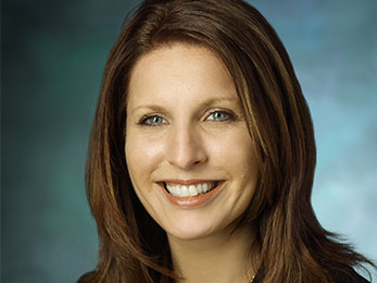 Stacy Colimore, in a formal portrait, wearing a black jacket, red shirt and pearl necklace